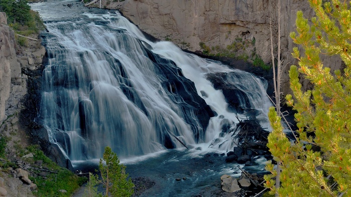 Waterfall cascading over dark rocks with pine trees