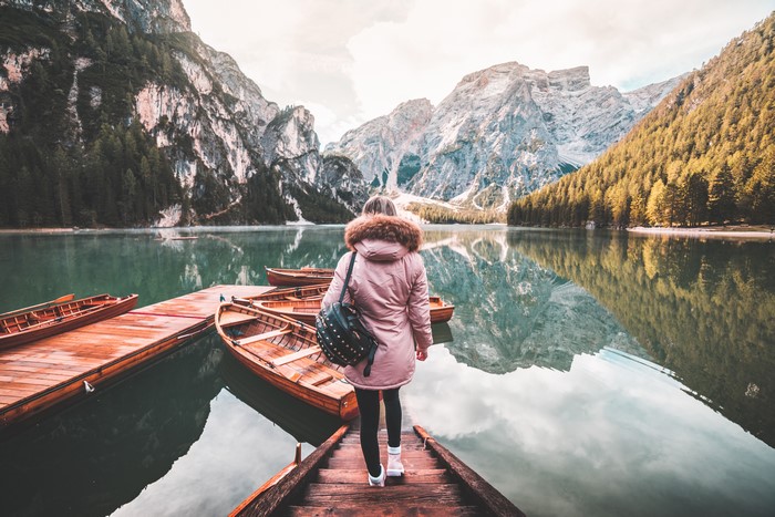 Woman with backpack on wooden pier with boats and mountains