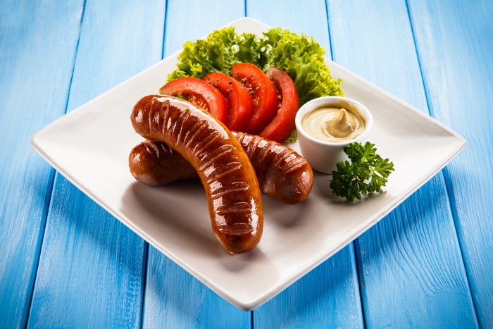 Sausages with tomatoes, lettuce, and mustard on a plate