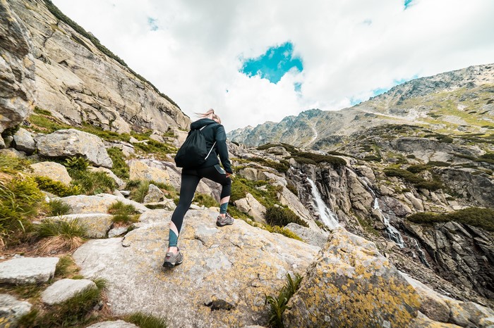 Blonde girl hiking up rocky mountain with waterfall