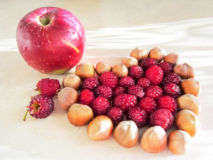 Red apple, raspberries, and hazelnuts on a table