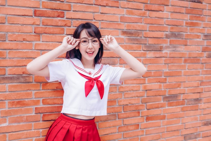 Asian girl in school uniform with glasses posing by brick wall