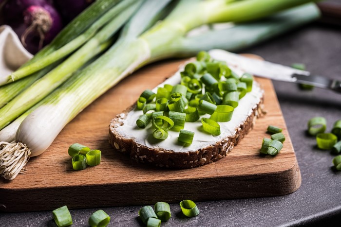 Scallions and bread with cream cheese on cutting board