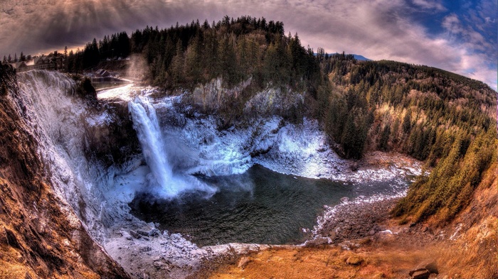 Waterfall cascading into a pool surrounded by trees and snow