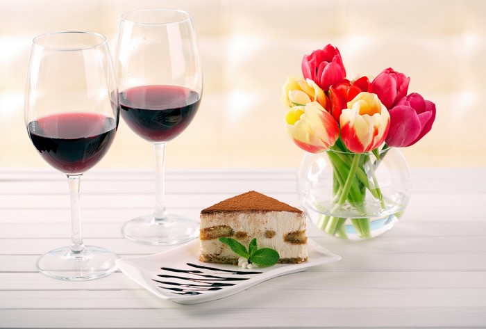 Two glasses of red wine, tiramisu, and tulips