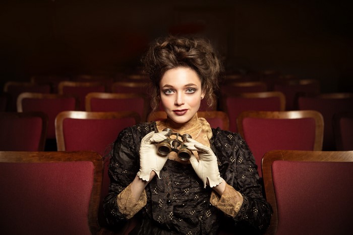 Woman in vintage dress holding opera glasses in theater