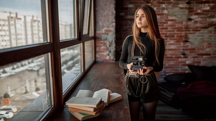 Woman with camera by window with books
