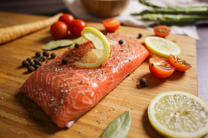 Salmon fillet with lemon, tomatoes, and spices on a cutting board