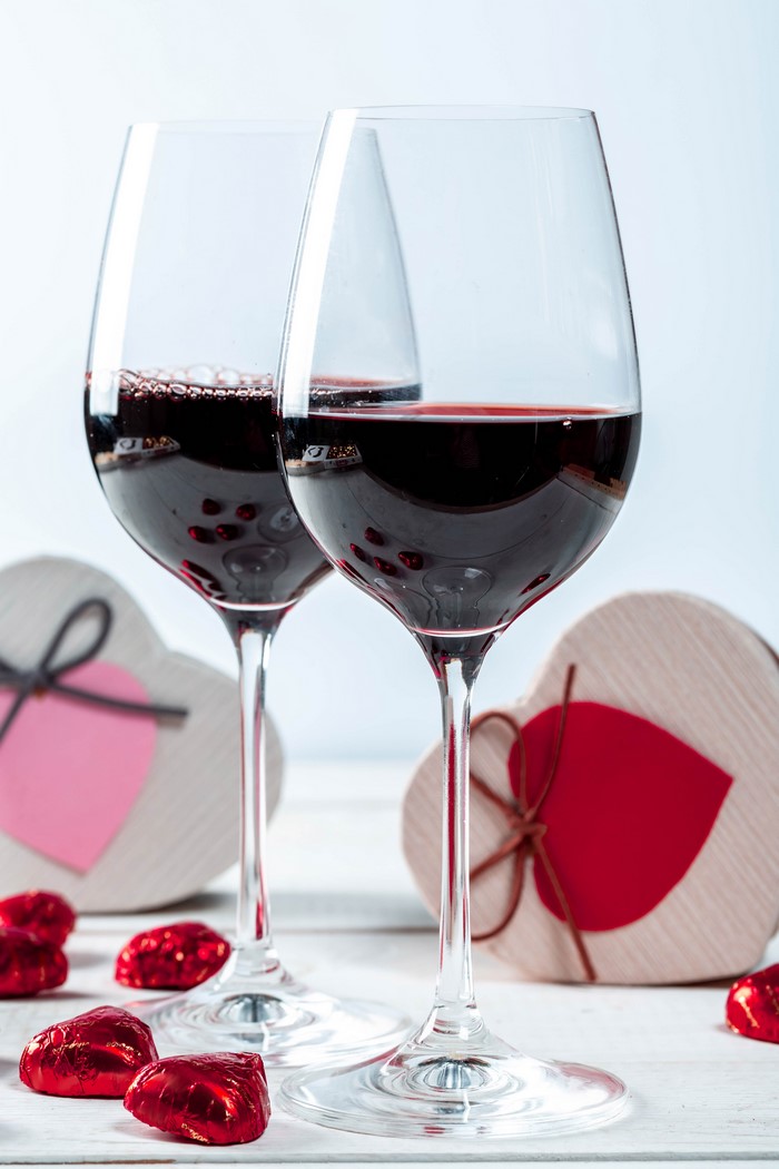 Two glasses of red wine with heart-shaped candies and gifts