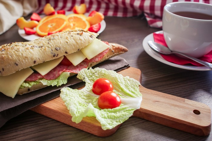 Sandwich with cheese, sausage, and vegetables on a cutting board