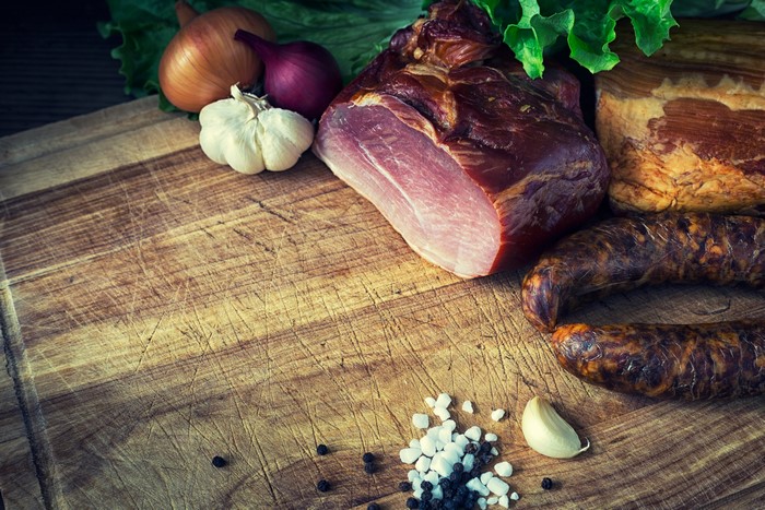 Meat products, ham, sausage, garlic, and onion on a cutting board
