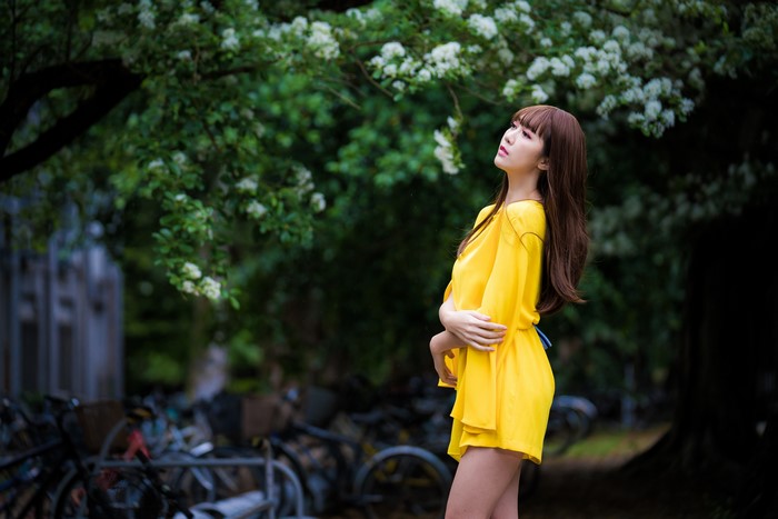 Asian woman in yellow dress posing near blooming tree