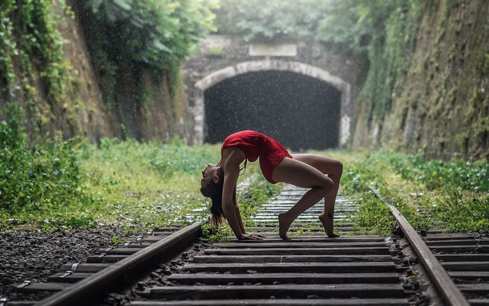 Woman in red leotard doing a backbend on train tracks