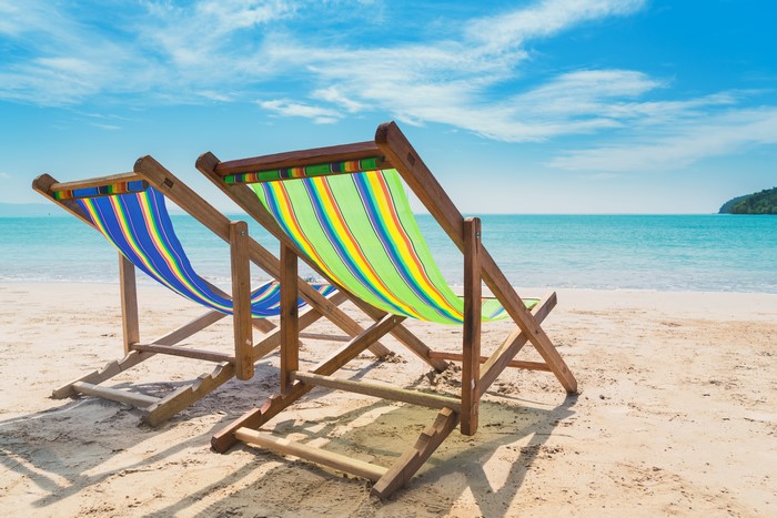 Two colorful beach chairs on a sandy beach with the ocean and sky in the background