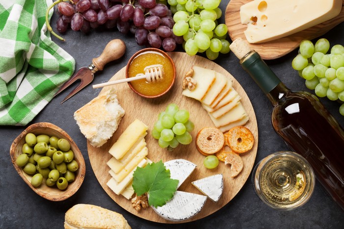 Cheese, Grapes, Olives, Honey, and Wine on a Cutting Board