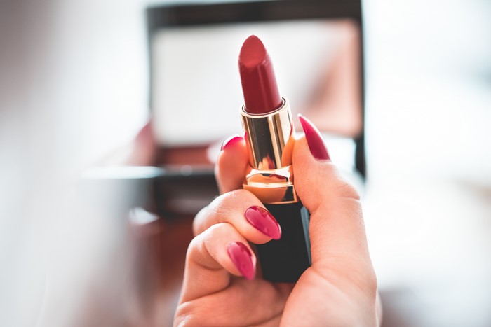Woman holding red lipstick with manicured nails