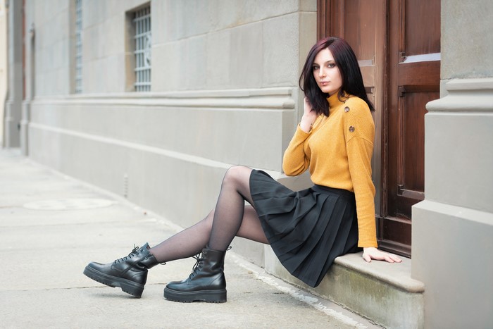 Elisa sitting on a step wearing a sweater and skirt