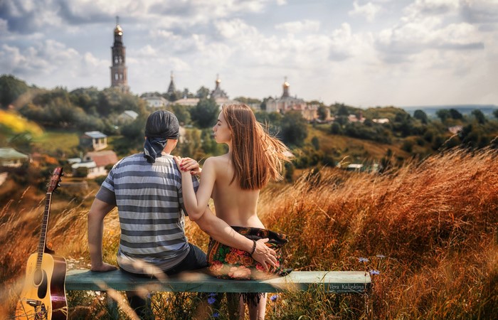 Couple sitting on bench with guitar and monastery
