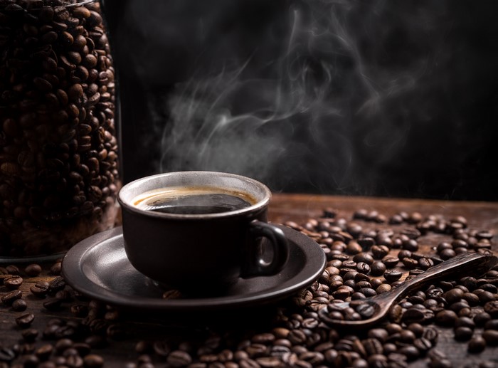 Steaming cup of coffee with coffee beans