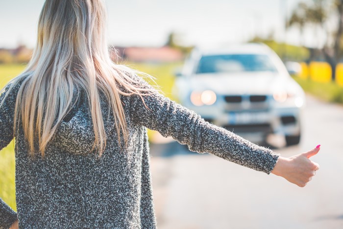 Blonde woman hitchhiking with a car approaching