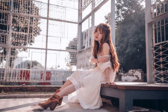 Asian woman with brown hair in a white dress sitting outdoors