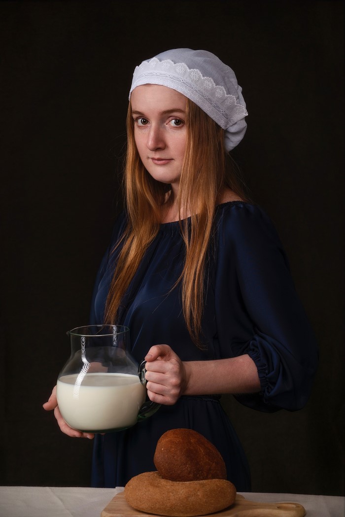 Redhead girl in a bonnet holding a jug of milk and bread