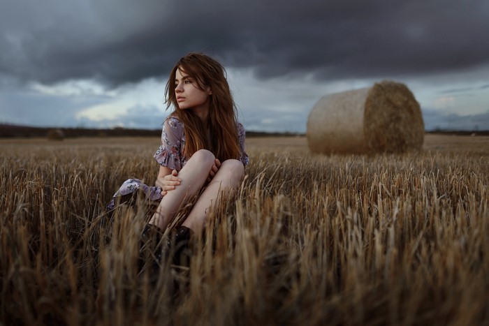 Aleks Five sitting in a field with a hay bale