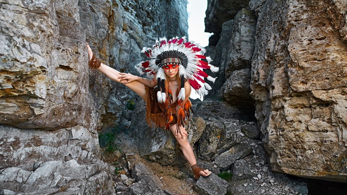 Woman in Native American Headdress Poses in Rocky Terrain