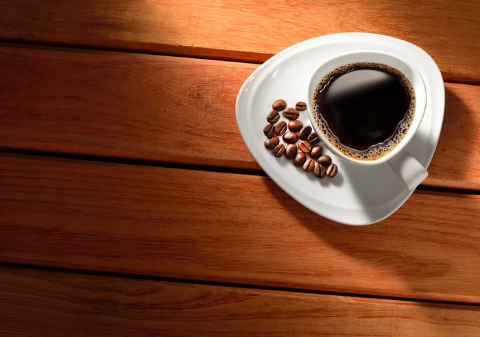 Coffee cup with beans on saucer on wood