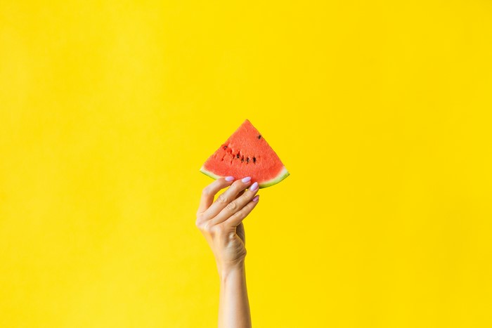 Hand holding a slice of watermelon on a yellow background