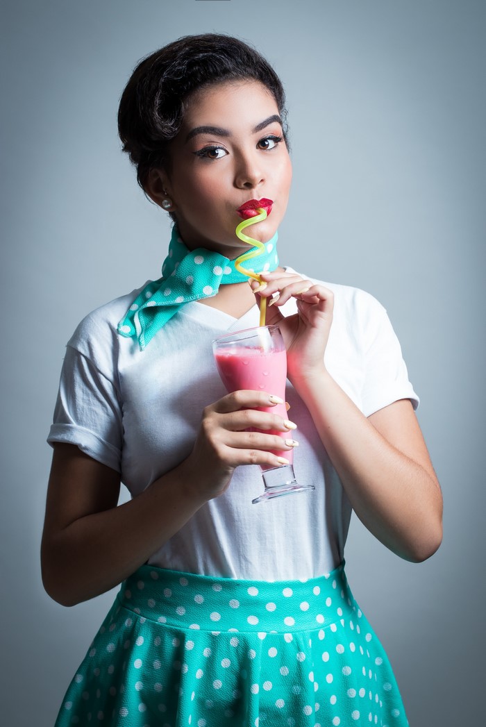 Brunette girl in retro outfit drinking a pink cocktail
