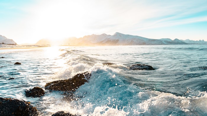 Waves crashing on rocks with mountains at sunset