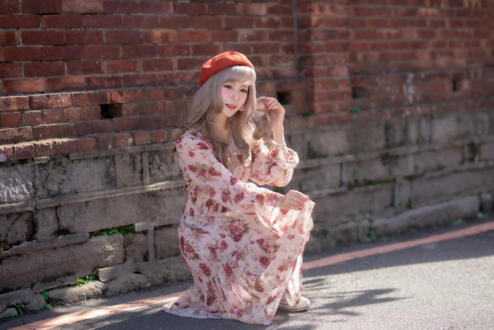 Asian woman in floral dress and beret posing by brick wall