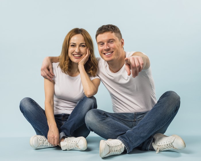 Couple sitting on floor pointing at camera