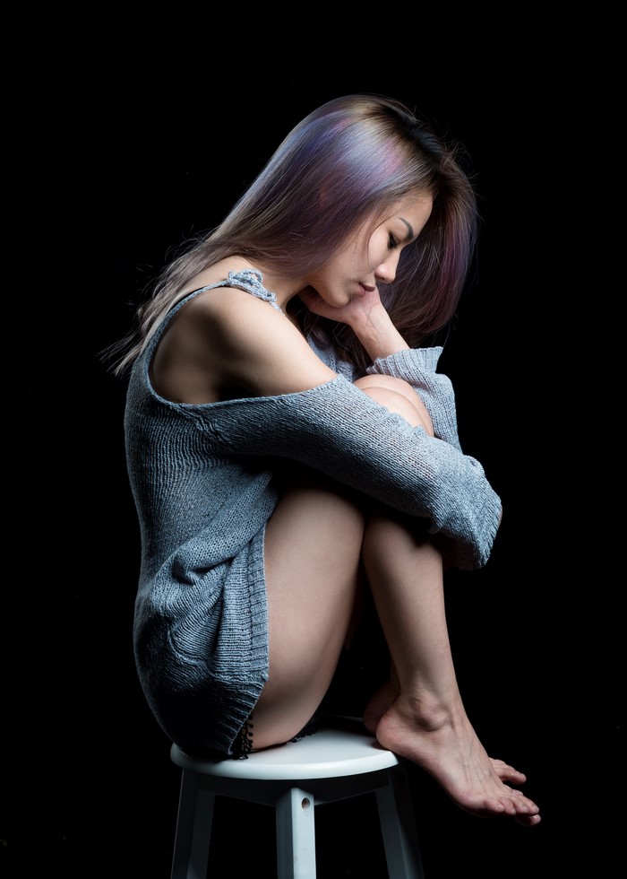 Asian woman sitting on stool with legs pulled up