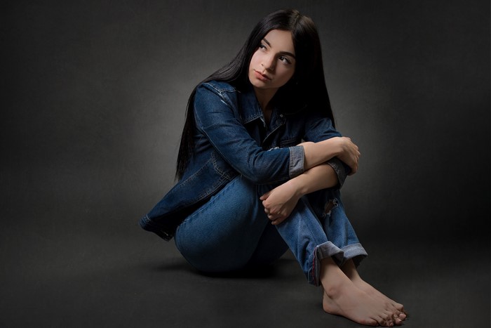 Brunette girl in denim jacket and jeans sitting on floor