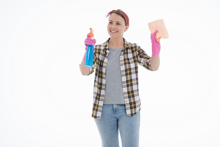 Woman in plaid shirt and jeans holding spray bottle and cloth