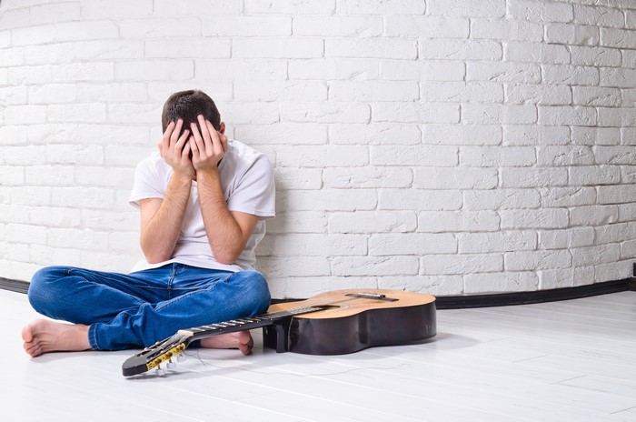 Man sitting with guitar, covering face