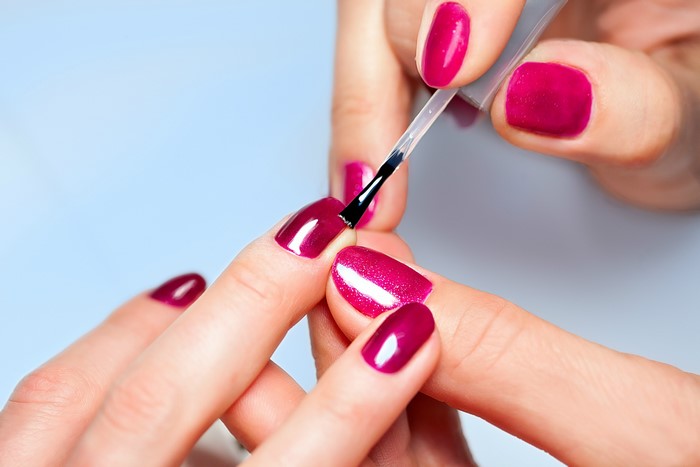 Applying dark pink nail polish to fingernails