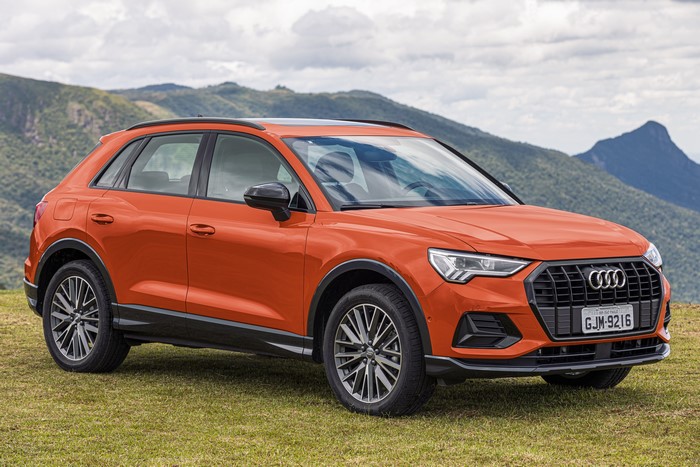 Orange Audi Q3 crossover parked on grass with mountains in background