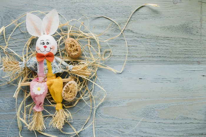 Easter bunny scarecrow with straw and eggs on wood