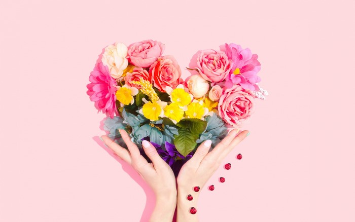 Heart-shaped flower bouquet held by hands with ladybugs