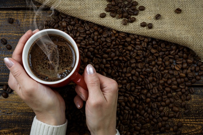 Hands holding a mug of coffee with coffee beans