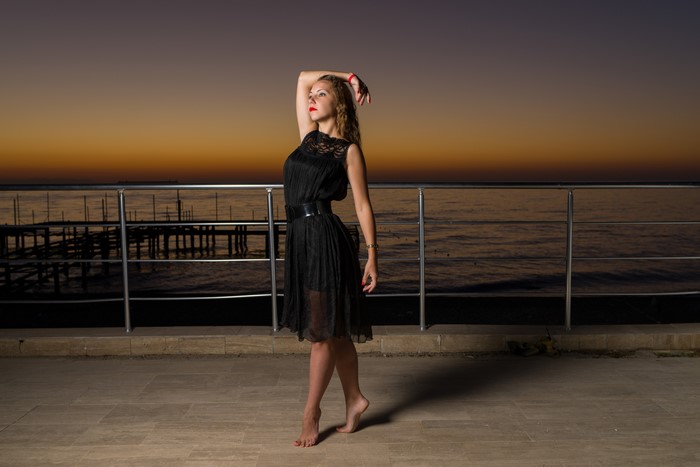 Woman in black dress on waterfront at sunset
