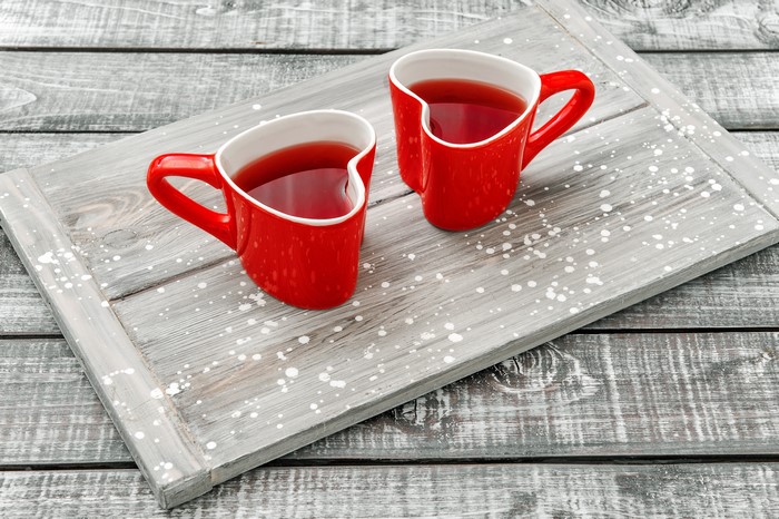 Two red heart-shaped mugs of tea on a tray