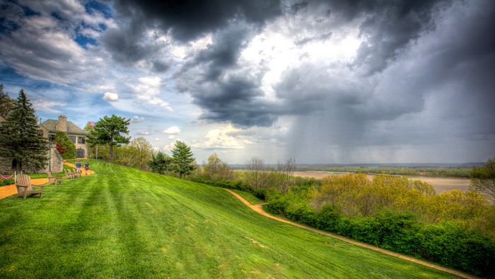 Lawn with chairs and building overlooking river under stormy sky
