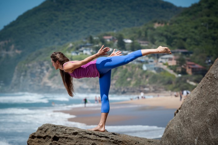 Woman performing yoga pose on a rock by the ocean
