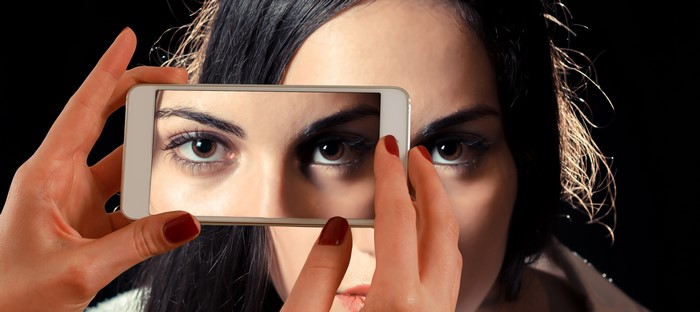 Woman holding smartphone showing her eyes