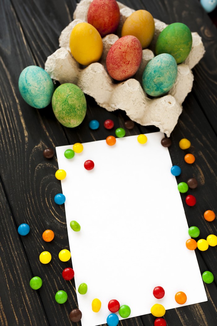 Easter eggs and candies on dark wood background with blank card