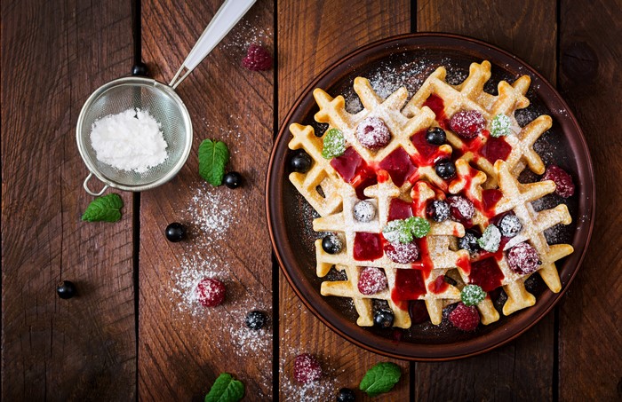 Waffles with berries and powdered sugar on wood planks